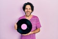 Handsome hispanic man holding vinyl disc celebrating crazy and amazed for success with open eyes screaming excited