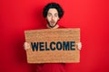 Handsome hispanic man holding welcome doormat afraid and shocked with surprise and amazed expression, fear and excited face Royalty Free Stock Photo