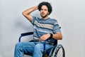 Handsome hispanic man sitting on wheelchair confuse and wondering about question Royalty Free Stock Photo
