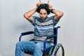 Handsome hispanic man sitting on wheelchair doing funny gesture with finger over head as bull horns