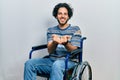 Handsome hispanic man sitting on wheelchair smiling with hands palms together receiving or giving gesture Royalty Free Stock Photo