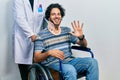 Handsome hispanic man sitting on wheelchair wearing neck collar showing and pointing up with fingers number five while smiling