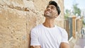 Handsome hispanic man smiling casually outdoors in a sunny urban setting, leaning against a textured wall Royalty Free Stock Photo