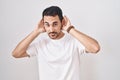 Handsome hispanic man standing over white background trying to hear both hands on ear gesture, curious for gossip Royalty Free Stock Photo