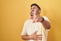 Handsome hispanic man standing over yellow background laughing at you, pointing finger to the camera with hand over body, shame Royalty Free Stock Photo