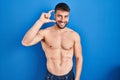 Handsome hispanic man standing shirtless smiling and confident gesturing with hand doing small size sign with fingers looking and Royalty Free Stock Photo