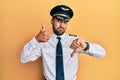 Handsome hispanic man wearing airplane pilot uniform doing thumbs up and down, disagreement and agreement expression