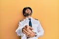 Handsome hispanic man wearing airplane pilot uniform laughing at you, pointing finger to the camera with hand over body, shame