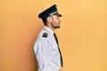 Handsome hispanic man wearing airplane pilot uniform looking to side, relax profile pose with natural face and confident smile