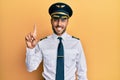 Handsome hispanic man wearing airplane pilot uniform showing and pointing up with finger number one while smiling confident and Royalty Free Stock Photo