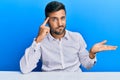 Handsome hispanic man wearing business clothes sitting on the table confused and annoyed with open palm showing copy space and Royalty Free Stock Photo