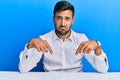 Handsome hispanic man wearing business clothes sitting on the table pointing down looking sad and upset, indicating direction with Royalty Free Stock Photo