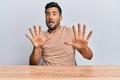 Handsome hispanic man wearing casual clothes sitting on the table afraid and terrified with fear expression stop gesture with Royalty Free Stock Photo