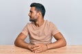 Handsome hispanic man wearing casual clothes sitting on the table looking to side, relax profile pose with natural face with Royalty Free Stock Photo