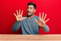 Handsome hispanic man wearing casual style sitting on the table afraid and terrified with fear expression stop gesture with hands, Royalty Free Stock Photo