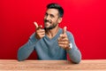 Handsome hispanic man wearing casual style sitting on the table pointing fingers to camera with happy and funny face Royalty Free Stock Photo