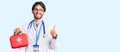Handsome hispanic man wearing doctor coat holding first aid kit smiling happy and positive, thumb up doing excellent and approval Royalty Free Stock Photo