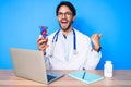 Handsome hispanic man wearing doctor uniform holding heart pointing thumb up to the side smiling happy with open mouth Royalty Free Stock Photo