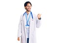 Handsome hispanic man wearing doctor uniform and stethoscope smiling with happy face looking and pointing to the side with thumb Royalty Free Stock Photo