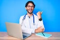 Handsome hispanic man wearing doctor uniform working at the clinic pointing thumb up to the side smiling happy with open mouth Royalty Free Stock Photo
