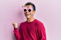 Handsome hispanic man wearing funny happy birthday glasses celebrating surprised and amazed for success with arms raised and eyes Royalty Free Stock Photo