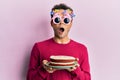 Handsome hispanic man wearing funny happy birthday glasses holding cake afraid and shocked with surprise and amazed expression, Royalty Free Stock Photo