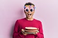 Handsome hispanic man wearing funny happy birthday glasses holding cake celebrating crazy and amazed for success with open eyes Royalty Free Stock Photo