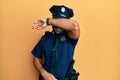 Handsome hispanic man wearing police uniform covering eyes with arm smiling cheerful and funny Royalty Free Stock Photo