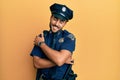 Handsome hispanic man wearing police uniform hugging oneself happy and positive, smiling confident