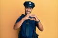 Handsome hispanic man wearing police uniform smiling in love doing heart symbol shape with hands