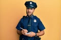 Handsome hispanic man wearing police uniform writing traffic fine clueless and confused expression