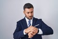 Handsome hispanic man wearing suit and tie checking the time on wrist watch, relaxed and confident Royalty Free Stock Photo