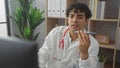 Handsome hispanic man in a white coat with a stethoscope records a message at a hospital workplace