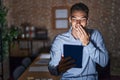 Handsome hispanic man working at the office at night laughing and embarrassed giggle covering mouth with hands, gossip and scandal Royalty Free Stock Photo