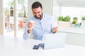 Handsome hispanic man working using computer laptop and drinking a cup of coffee screaming proud and celebrating victory and Royalty Free Stock Photo
