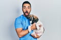 Handsome hispanic veterinary man with beard checking dog health afraid and shocked with surprise and amazed expression, fear and Royalty Free Stock Photo