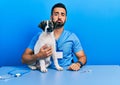 Handsome hispanic veterinary man with beard checking dog health depressed and worry for distress, crying angry and afraid Royalty Free Stock Photo