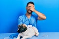 Handsome hispanic veterinary man with beard checking dog health smiling and laughing with hand on face covering eyes for surprise Royalty Free Stock Photo