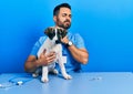 Handsome hispanic veterinary man with beard checking dog health touching painful neck, sore throat for flu, clod and infection Royalty Free Stock Photo