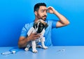 Handsome hispanic veterinary man with beard checking dog health very happy and smiling looking far away with hand over head Royalty Free Stock Photo