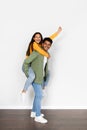 Handsome indian man giving piggyback ride to his wife against white studio wall, full length, vertical shot Royalty Free Stock Photo