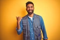 Handsome indian technician man wearing uniform over isolated yellow background smiling with happy face looking and pointing to the