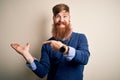 Handsome Irish redhead business man with beard standing over isolated background amazed and smiling to the camera while presenting Royalty Free Stock Photo
