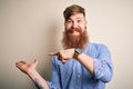 Handsome Irish redhead business man with beard standing over isolated background amazed and smiling to the camera while presenting Royalty Free Stock Photo