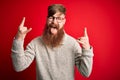 Handsome Irish redhead man with beard wearing casual sweater and glasses over red background shouting with crazy expression doing Royalty Free Stock Photo