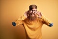 Handsome Irish redhead man with beard wearing glasses over yellow isolated background Trying to hear both hands on ear gesture, Royalty Free Stock Photo