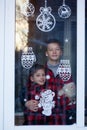 Handsome Kids standing by the decorated window with a toy santa claus and look and wait Christmas eve. Children hug and enjoy the Royalty Free Stock Photo