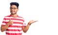 Handsome latin american young man wearing casual clothes and glasses showing palm hand and doing ok gesture with thumbs up, Royalty Free Stock Photo