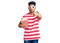 Handsome latin american young man wearing 3d glasses and eating popcorn at the movies pointing with finger to the camera and to