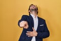 Handsome latin man standing over yellow background laughing at you, pointing finger to the camera with hand over body, shame Royalty Free Stock Photo